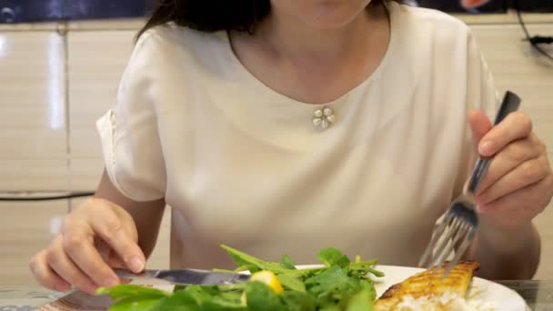 Vrouw eet koekenvis met groene bladeren zittend in café, handen close-up. — Stockvideo