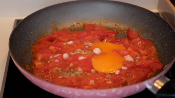 Woman cooks fried eggs with tomatoes in skillet at home kitchen, hands closeup. — Stock Video