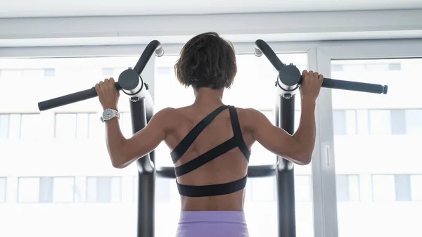 Mogen kvinna gör pull-ups med brett grepp i gymmet, back View. — Stockfoto
