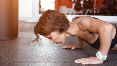Atletik olgun kadın spor salonunda yerden reps şınav seti yapıyor.