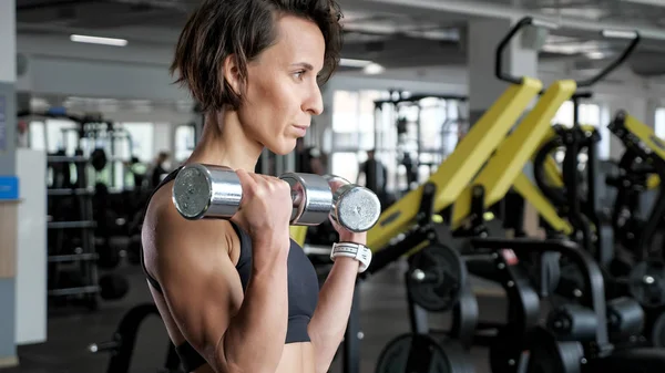 Sportowy dojrzała kobieta robi biceps ćwiczenia z hantlami w siłowni. — Zdjęcie stockowe