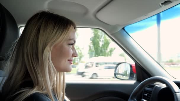 Mujer joven rubia conduce un coche en la ciudad cogido de la mano en el volante . — Vídeos de Stock