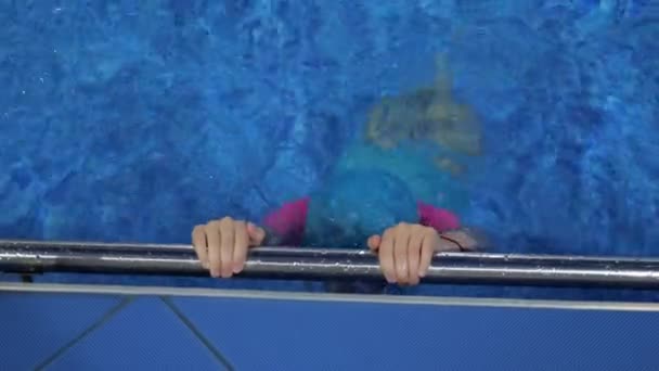 Menina está mergulhando subaquático na piscina segurando no corrimão de metal . — Vídeo de Stock