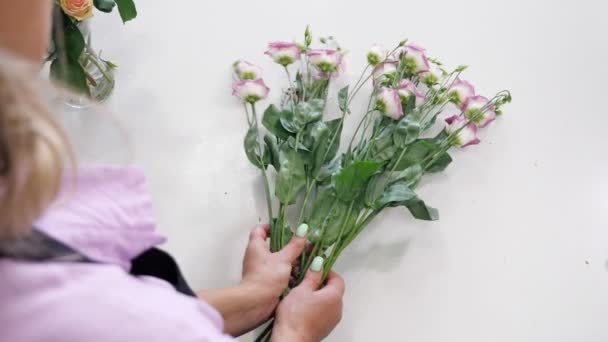 Woman florist works with white and purple flowers on the table, hands closeup.