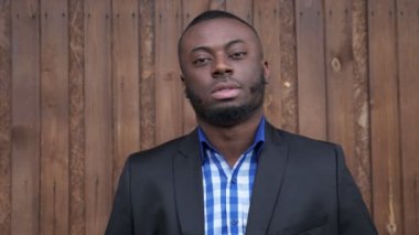 Afro amerikan adam takım gülümseyerek ve koyu ahşap arka plan üzerinde kamera bakıyor.