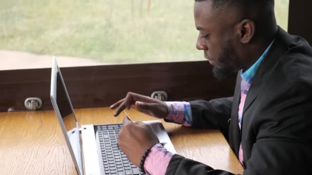 Homem preto faz pagamento cartão bancário no laptop compra on-line, compras senta-se no café . — Vídeo de Stock