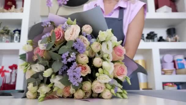 Florista é buquê de embalagem de rosas e folhas em papel, mãos de close-up . — Vídeo de Stock