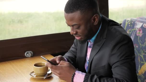 Afro american businessman is typing a message on smartphone sitting in cafe. — Stock Video