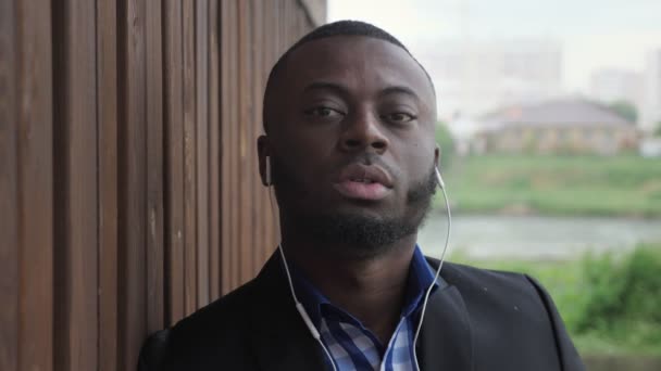 Homem negro em fones de ouvido está ouvindo música na rua da cidade durante a chuva . — Vídeo de Stock