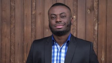 Afro amerikan adam takım gülümseyerek ve koyu ahşap arka plan üzerinde kamera bakıyor.