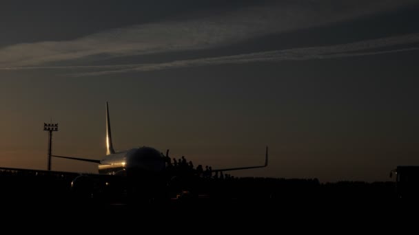 乗客のシルエットは、夕方に着陸の準備をする航空機に近づく. — ストック動画