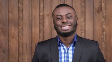 Afro amerikan adam takım gülümseyerek ve koyu ahşap arka plan üzerinde kamera bakıyor.