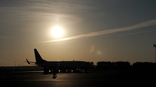 El avión comienza a moverse en la pista y los trabajadores salen de la pista de aterrizaje, siluetas al atardecer . — Vídeos de Stock