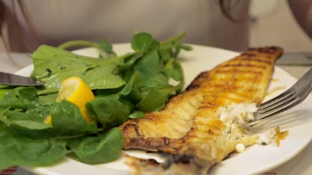 Woman is eating frying fish with green leaves sitting in cafe, hands closeup. — Stock Video