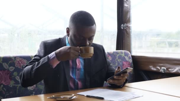 Afro american businessman is typing a message on smartphone sitting in cafe. — Stock Video