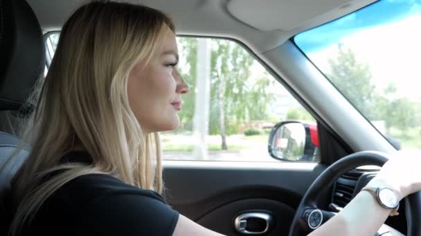 Blonde young woman is driving a car in the city holding hands on steering wheel. — Stock Video