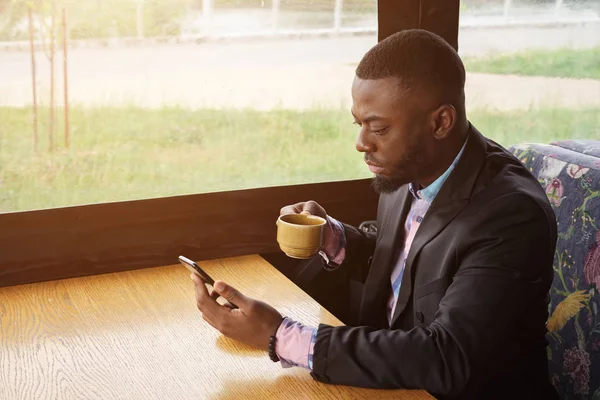 Afro americano uomo d'affari sta digitando un messaggio su smartphone seduto nel caffè . — Foto Stock