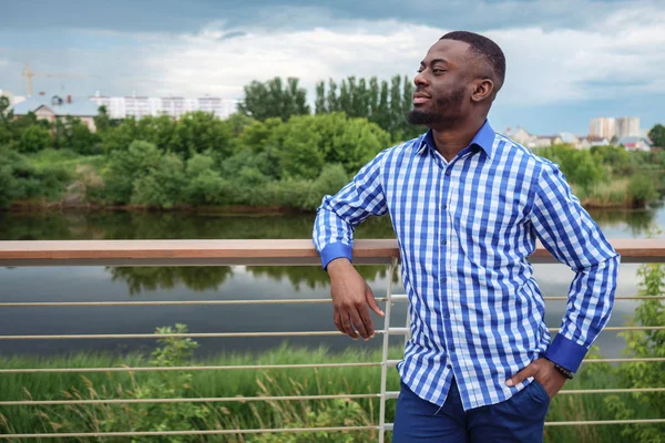 Black man smiles and stands on waterfront in park. — Stock Photo, Image