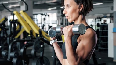 Sportif olgun kadın spor salonunda dumbbells ile pazı egzersiz yapıyor.