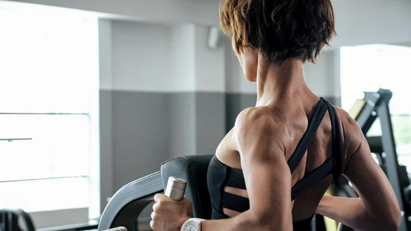 Mulher esportiva está fazendo exercícios para os músculos da coluna no simulador de bloqueio — Fotografia de Stock