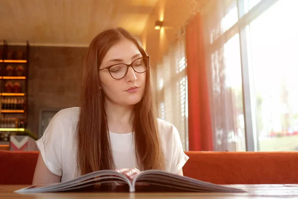 Smiling beautiful girl in glasses looking menu in cafe.