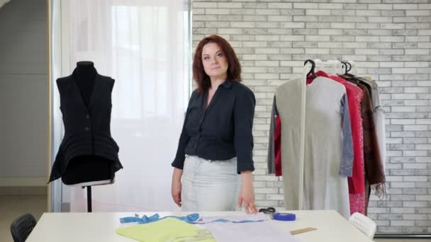 Retrato de mujer madura diseñador de moda mira a la cámara y sonríe en el taller . — Vídeo de stock