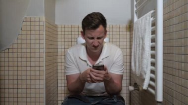 tuvalette akıllı telefon kullanan adam.
