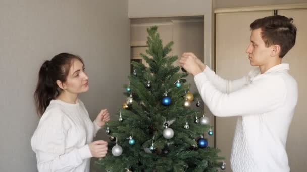 Handsome young man and pretty lady decorate christmas tree — Stock Video