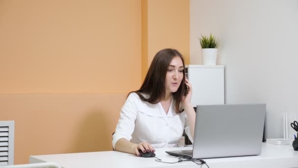 Leende Lady receptionist samtal på smartphone på laptop — Stockvideo
