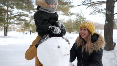 Genç aile, anne, oğul ve baba kış şehir parkında bir kardan adam inşa ediyoruz.