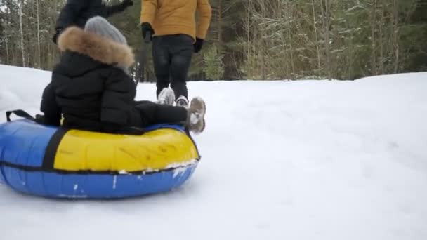 幸せな両親は、冬の公園でチューブで彼らの息子を実行し、スライドしています. — ストック動画