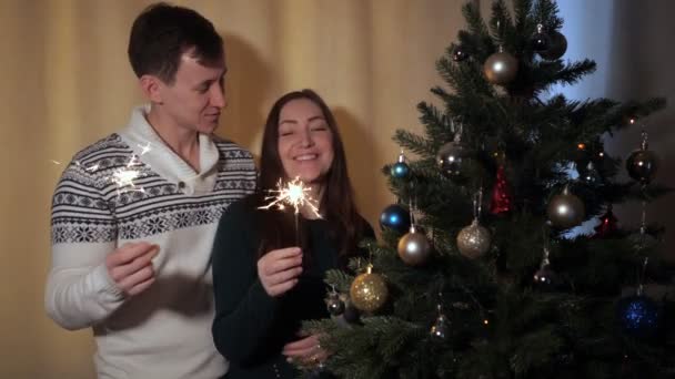 Hombre y hermosa dama cantar con bengalas por árbol de Navidad — Vídeos de Stock