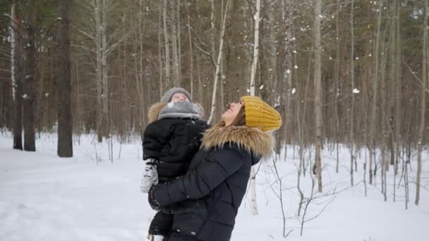 Jonge moeder met een kleine zoon in haar handen is op zoek naar sneeuwval in winter bos. — Stockvideo