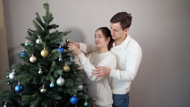 Hombre está detrás de señora ayuda a decorar árbol de Navidad — Vídeos de Stock