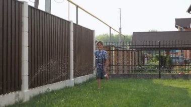 şort mutlu çocuk fıskiye ile yeşil bahçe boyunca çalışır