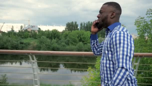 Black man calls on smartphone walking on waterfront in city park in slow motion. — Stock Video