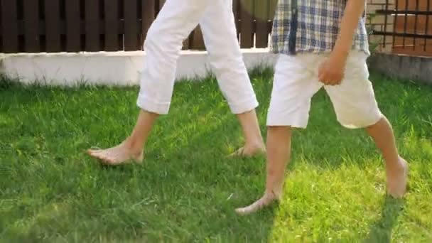 スリムな母と小さな男の子の足は、緑の芝生の上を裸足で歩きます — ストック動画