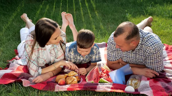 Šťastní členové rodiny leží na břiše na červené přikrývce při pikniku — Stock fotografie