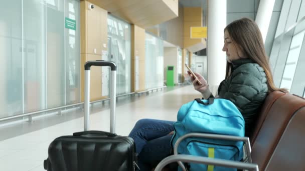 Mujer en el aeropuerto está esperando su vuelo, algo mirando el teléfono inteligente . — Vídeos de Stock