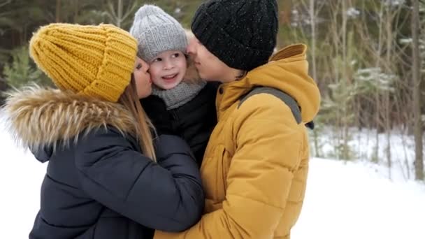 Anya és apa is hozzábújva és megcsókolta a kisfiát a téli parkban. — Stock videók