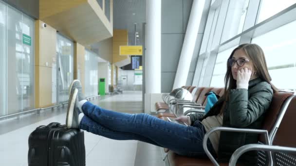 Mujer joven aburrida está esperando su vuelo en el aeropuerto sentado en el pasillo . — Vídeo de stock