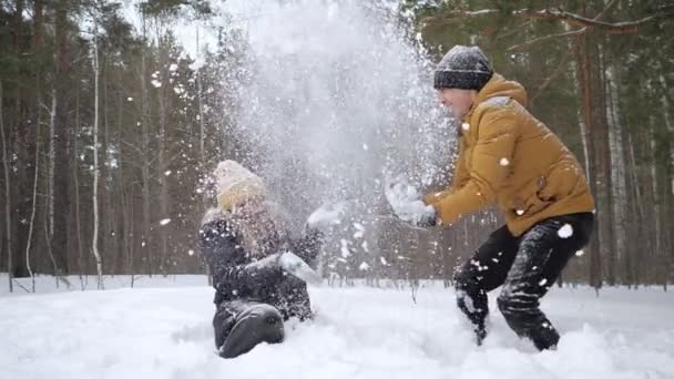 Para, dziewczyna i facet, rzucają śnieg siebie w lesie zimowym w zwolnionym tempie. — Wideo stockowe