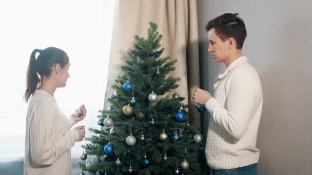 Handsome young man and pretty lady decorate christmas tree — Stock Video