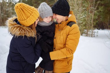 Anne ve baba kış parkında küçük oğullarına sarılıp öpüşüyorlar..