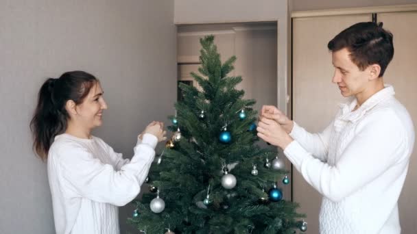Handsome young man and pretty lady decorate christmas tree — Stock Video