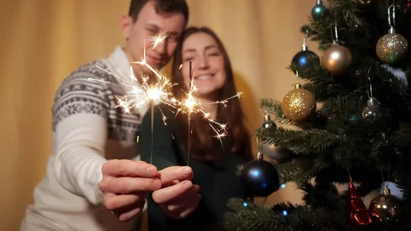 Happy couple in sweaters hold bright sparklers near camera — Stock Photo, Image