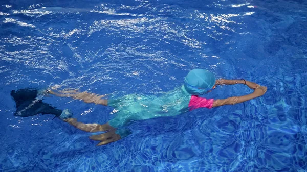 Маленькая девочка в купальнике, кепке и очках ныряет и плавает к яйцу бассейна . — стоковое фото