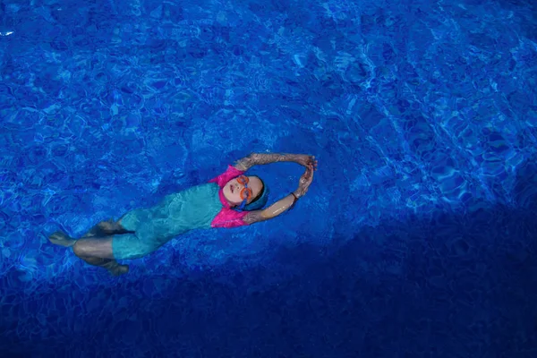 Enfant fille en lunettes, maillot de bain et casquette s'entraîne à nager dans la piscine . — Photo