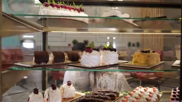 Happy couple chooses tasty cakes in glass show case of shop — Stock Video