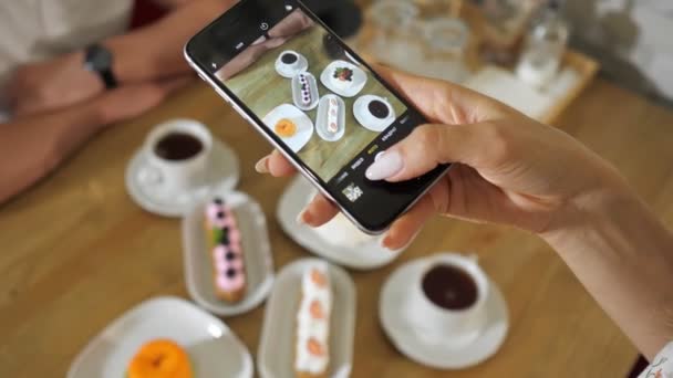 Femme prend des photos de délicieux gâteaux et thé sur une table en bois — Video